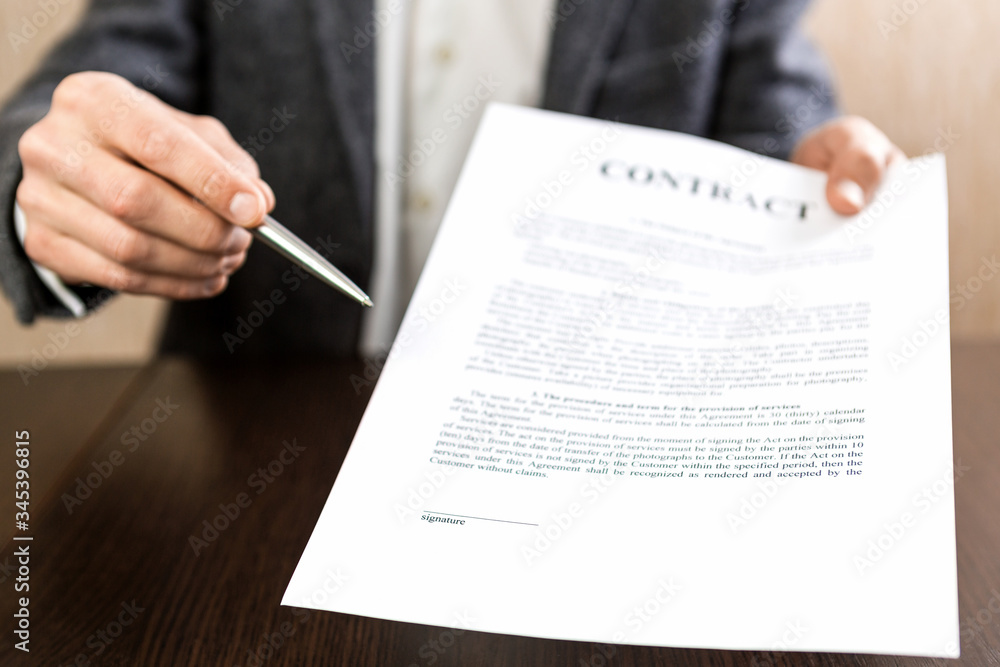 Businessman handing over a contract for signature offering a ballpoint pen in his hand Businessman handing over a contract for signature offering a ballpoint pen in his hand
