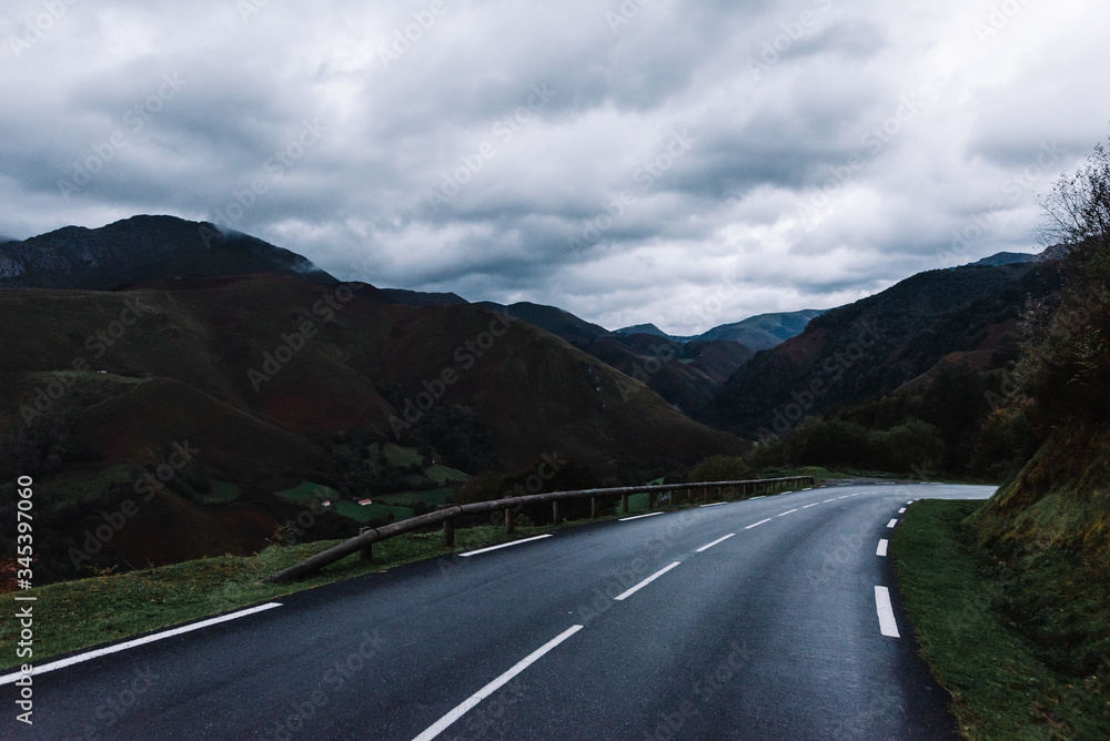 Picturesque image of rural road between dark green mountains on a wet and cloudy gray day