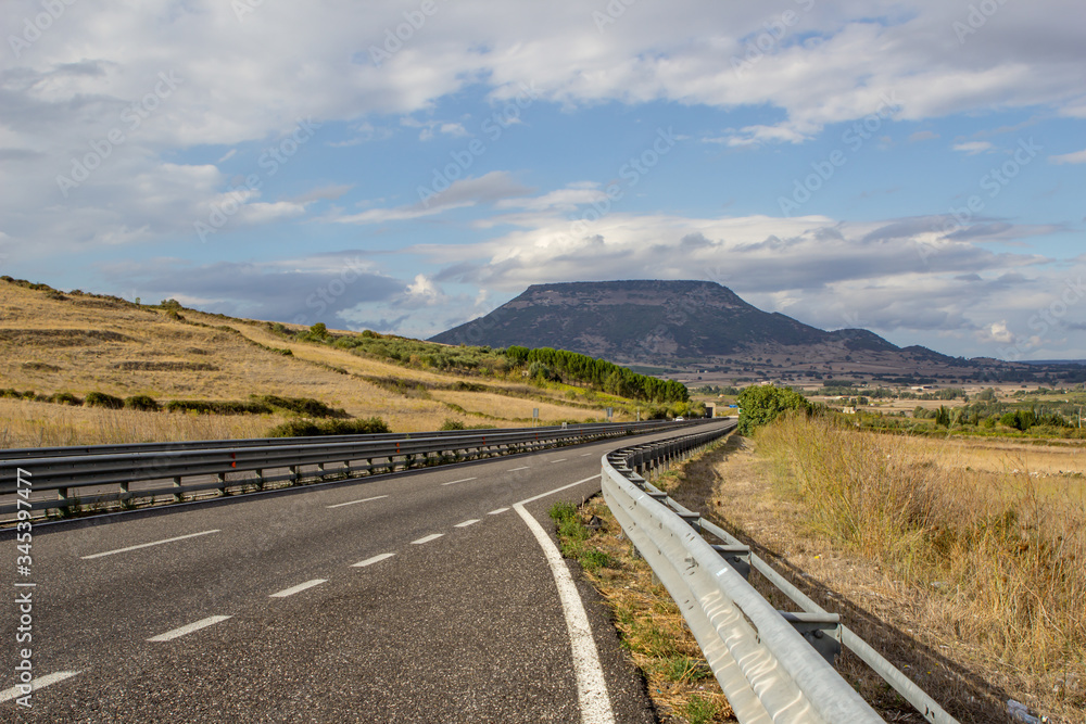 Sunny sky with clouds and beautiful asphalt road with crash barrier. Green hills, fields with grass. Beautiful landscape in Sardinia in summer, Italy. Sunny sky with clouds and beautiful asphalt road with crash barrier. Green hills, fields with grass. Beautiful landscape in Sardinia in summer, Italy.