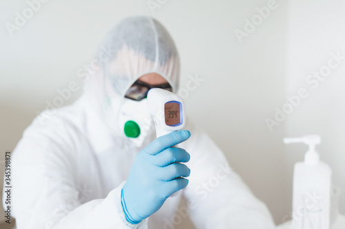 Medical professionals coronavirus risk concept. Doctor with fever in protective clothing measuring himself for Covid-19 in the hospital.