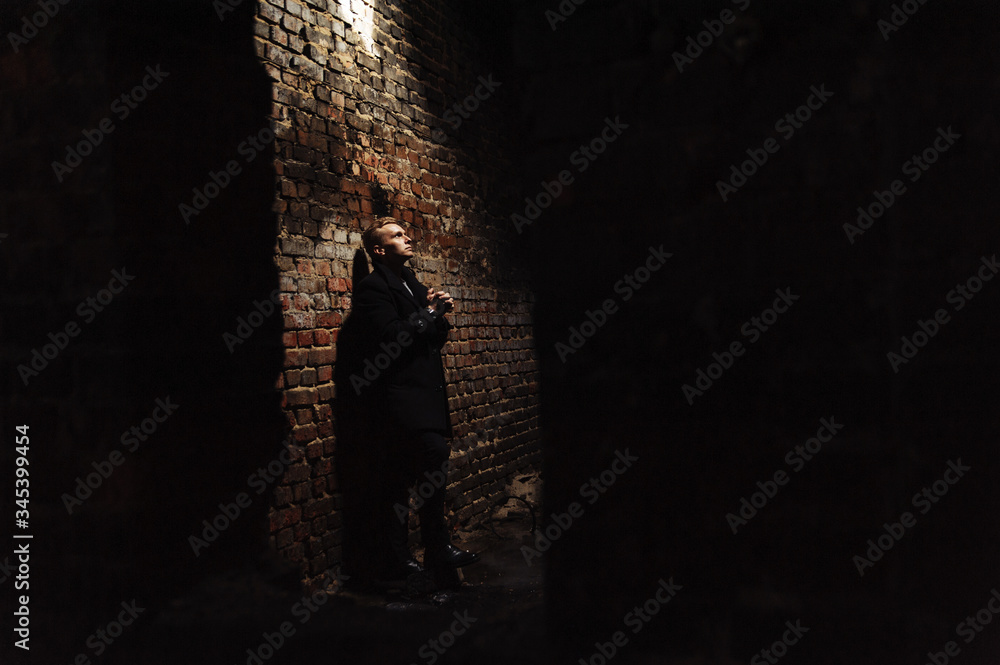 Young man standing near the wall in the abandoned buiding under light ray