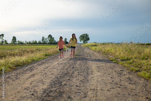 Authentic shot of two carefree happy little girls are having fun to run together their Labrador puppy on a countryside  road in a sunny day. Concept: love for animals and nature, happiness, freedom