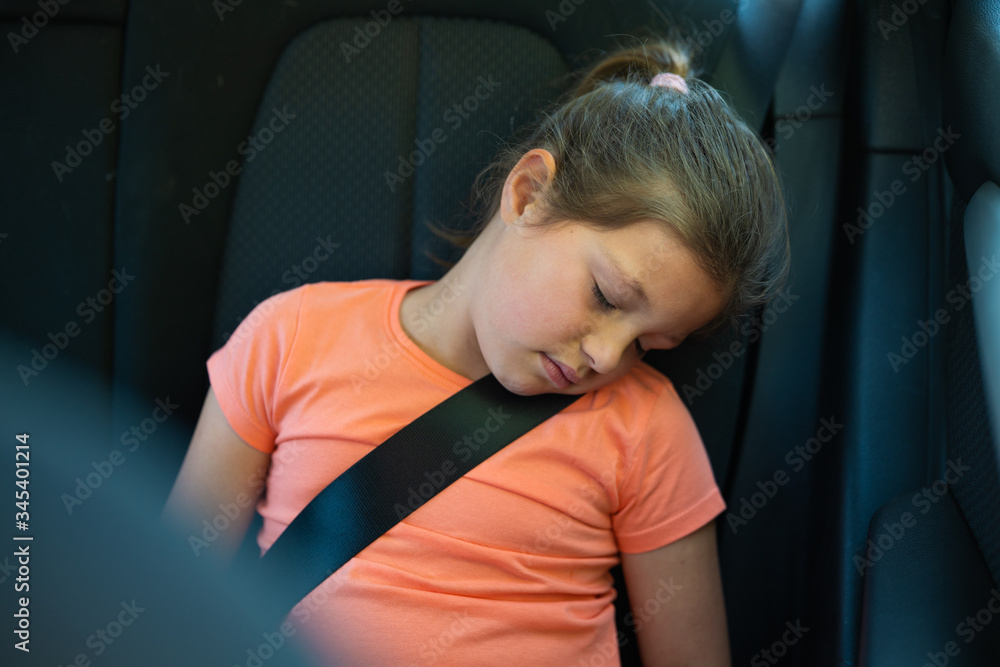 Authentic shot of a preschooler girl is sleeping in a backseat of a car locked with safety belt during traveling with family. Concept: family, travel, security, journey, safety, comfort