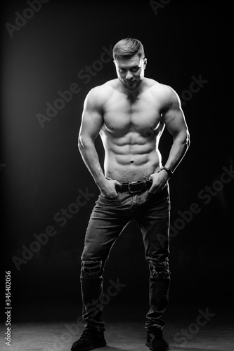 A portrait of a hot handsome strong guy man without a shirt against dark background. Hands on belt. Studio photo. Male beauty concept. Black and white photo. Closeup. © Vadim