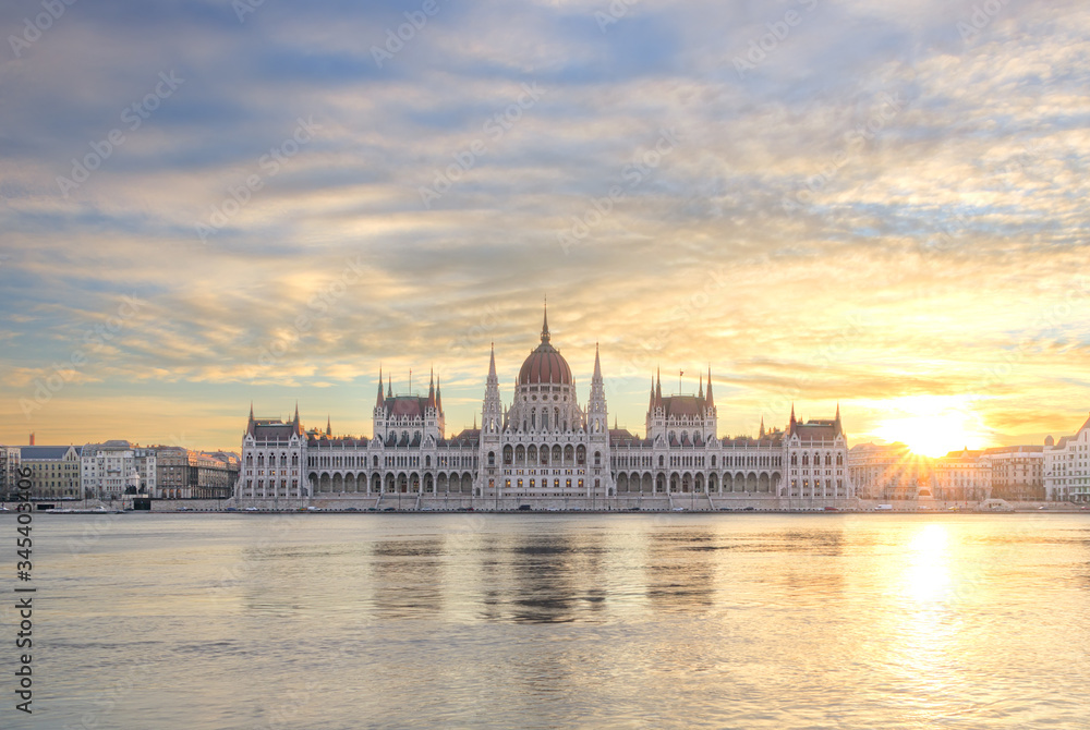 Hungarian Parliament at sunrise across the Danube in Budapest with colorful cloudy sky and sun rays