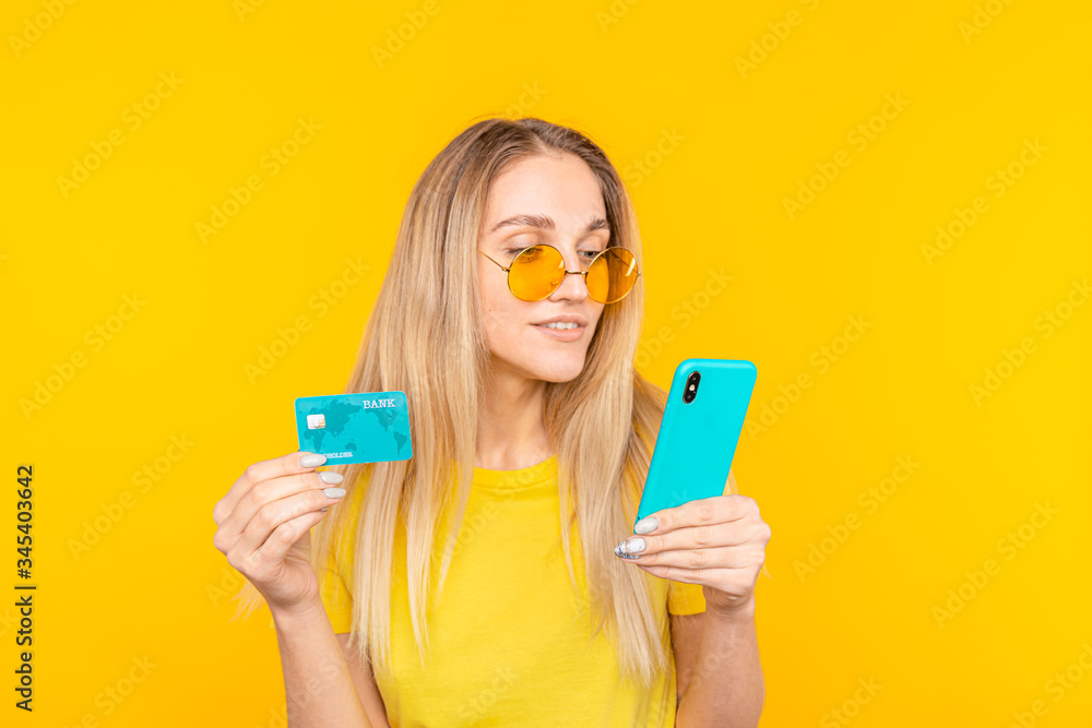 Portrait of a young blonde girl in sunglasses showing plastic credit card while using mobile phone. Portrait of a young blonde girl in sunglasses showing plastic credit card while using mobile phone.