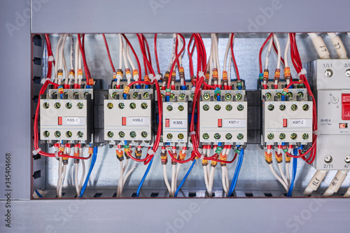 Several contactors and an automatic switch are arranged in a row in the electrical Cabinet. Wires are connected to the contactors. Front additional contacts are located on the front of the starters.