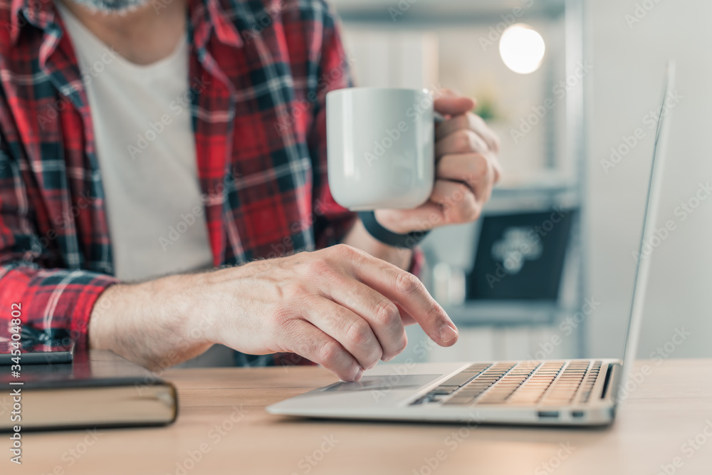 Freelancer using laptop computer and drinking coffee in home office Freelancer using laptop computer and drinking coffee in home office