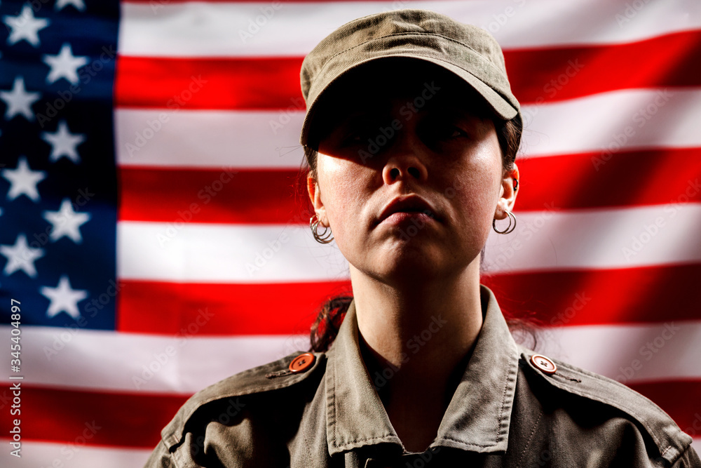 Veterans Day, Memorial Day. A portrait of a female soldier in uniform, against the background of the American flag. The concept of the American national holidays and patriotism Veterans Day, Memorial Day. A portrait of a female soldier in uniform, against the background of the American flag. The concept of the American national holidays and patriotism