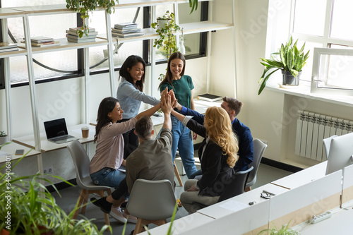 Happy diverse interns with female leader, coach giving high five at company meeting. Smiling woman mentor with employees celebrating achievement, team building activity. photo