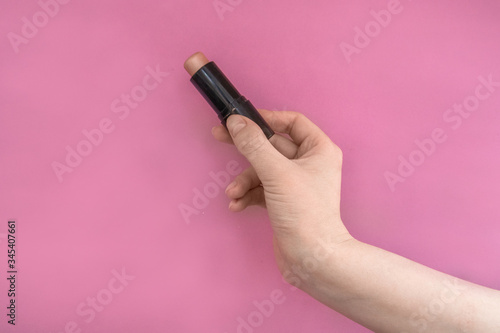 Highlighter for sculpting in a woman's hand on a pink background. Advertising.