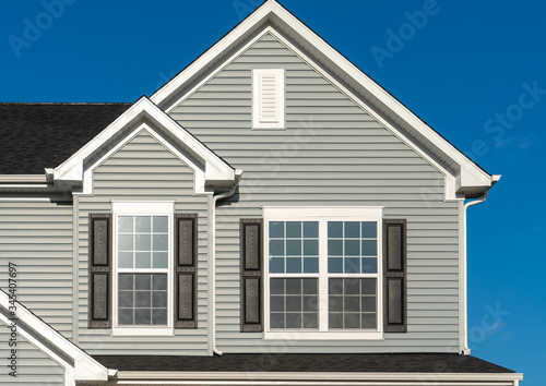 Classic American real estate single family home facade with horizontal vinyl siding, double gable, double and single sash windows, decorative white attic window blue sky background
