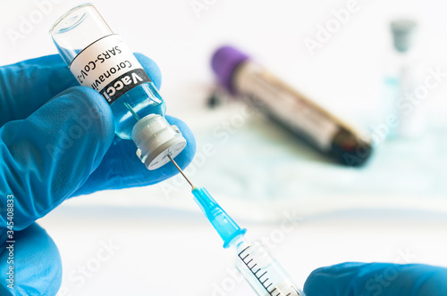 Coronavirus COVID-19 vaccine vial and injection syringe in medic hands concept.