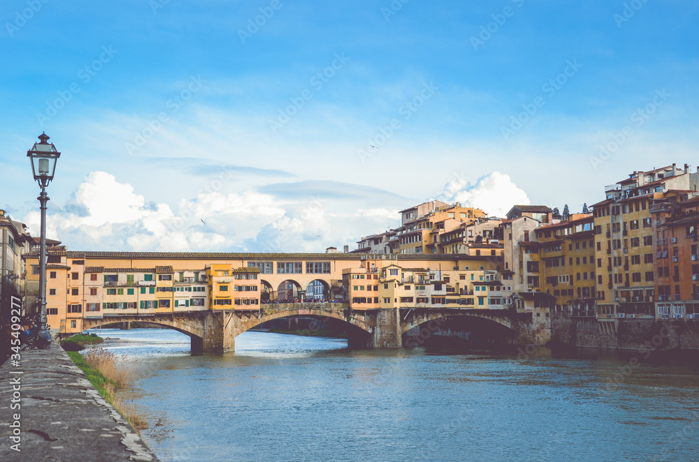 Famous Ponte Vecchio Bridge, medieval stone bridge over the Arno River in Florence, Tuscany, Italy. Major landmark of the Italian city. Blue sky, clouds in the background. Amazing cityscape