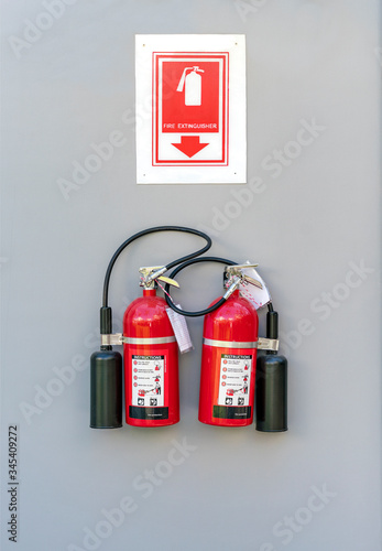 Two red fire extinguishers hanging on a white wall.