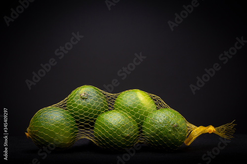 Green and yellow lime fruit in netting bag contrasted against a dark grey background. Studio low key vibrant product still life. photo