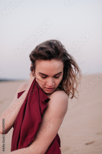 portrait of a young slender girl in a red dress in the wind in the desert