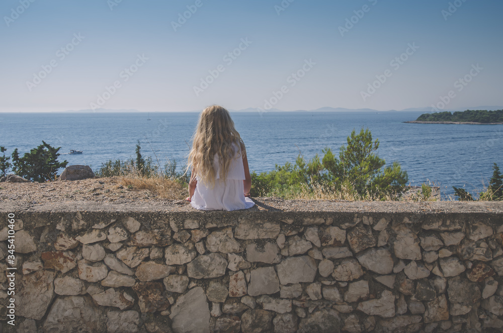 sad girl with long blond hair sitting alone back view by the sea and waiting