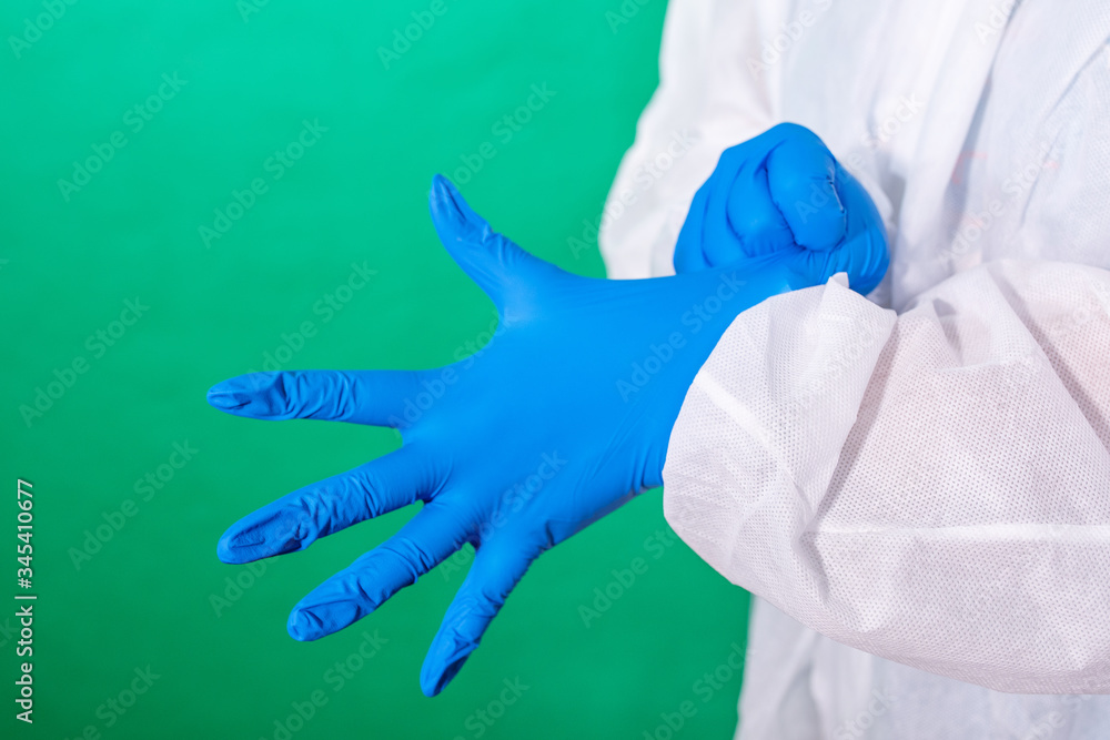COVID-19. Facial masks on the pile. Epidemic background. Close up of female doctor's hands putting on blue sterilized surgical gloves in the office. COVID-19. Facial masks on the pile. Epidemic background. Close up of female doctor's hands putting on blue sterilized surgical gloves in the office.