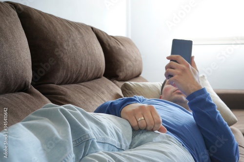 Young man using smartphone while lying on sofa