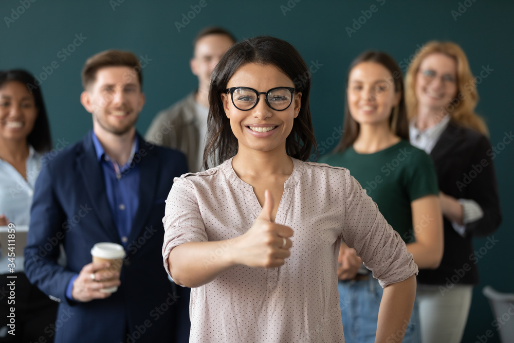 Portrait of african american businesswoman like gesture, showing thumbs up at camera. Different age diverse businesspeople standing behind of female company chief. Leader of multi-ethnic team concept Portrait of african american businesswoman like gesture, showing thumbs up at camera. Different age diverse businesspeople standing behind of female company chief. Leader of multi-ethnic team concept