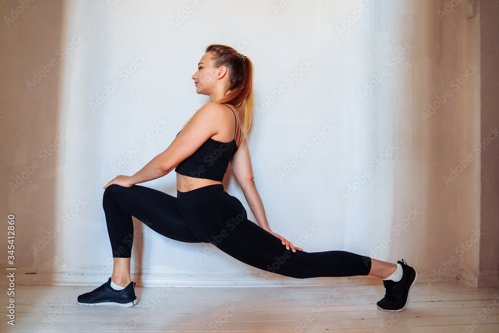 That's how it should be! Flexible, muscular, athlete girl does stretching, lifting leg up to the wall. Fitness trainer making a twine at home in the bedroom. Conducting live broadcasts for students That's how it should be! Flexible, muscular, athlete girl does stretching, lifting leg up to the wall. Fitness trainer making a twine at home in the bedroom. Conducting live broadcasts for students