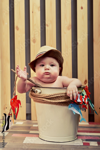 a small child in a straw hat sits in a bucket with a fishing rod photo