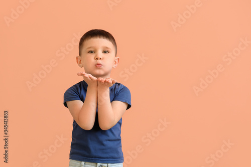 Cute little boy blowing kiss on color background