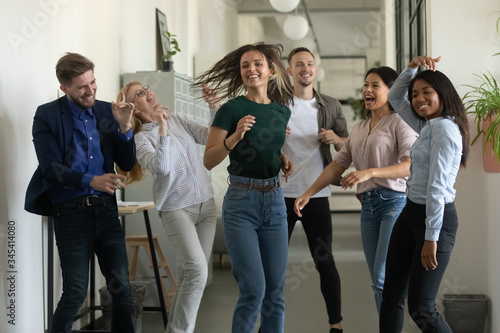 Happy young businesswoman and businessman dancing after successful deal. Diverse smiling employee energy moving for break and relaxing. Overjoyed motivated carefree multiracial business team. © fizkes