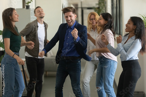 Happy young businessman mentor and woman dancing after successful deal. Diverse smiling relaxing employee energy moving for break. Overjoyed motivated carefree multiracial business team.