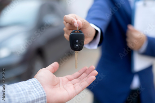 Close up of dealer giving key to new owner and shaking hands in auto show.