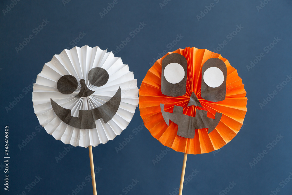 Obraz premium Two different folded paper decorations (smiling skull and Jack-o'-lantern) on the blue background. DIY Halloween decoration theme.