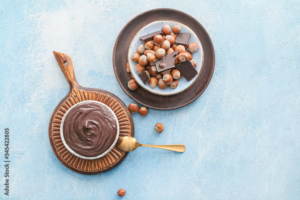 Fototapeta premium Plates with tasty chocolate paste and hazelnuts on color background
