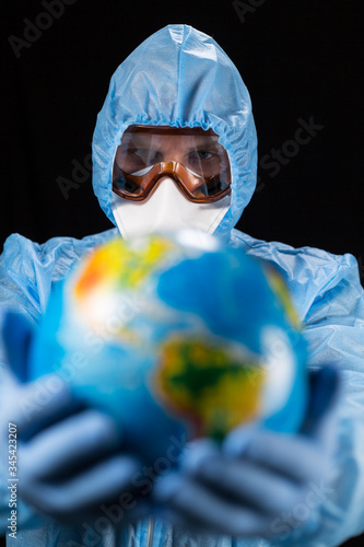 a man in a chemical protection suit and medical gloves holds a planet in his hands  a pandemic in the hands of a man. Save the nature. close-up