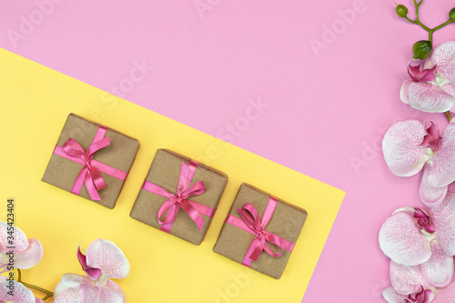flatlay of Gift present boxes with pink ribbon, orchid flowers on pink yellow background. spring concept. Copy space © olga_demina