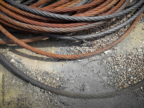 Old rusty strong cable rolled into the bay. The rings of iros are located on the ground, the yard of the enterprise. Solar lighting. Color image. Picture taken in Ukraine, Kiev region. photo