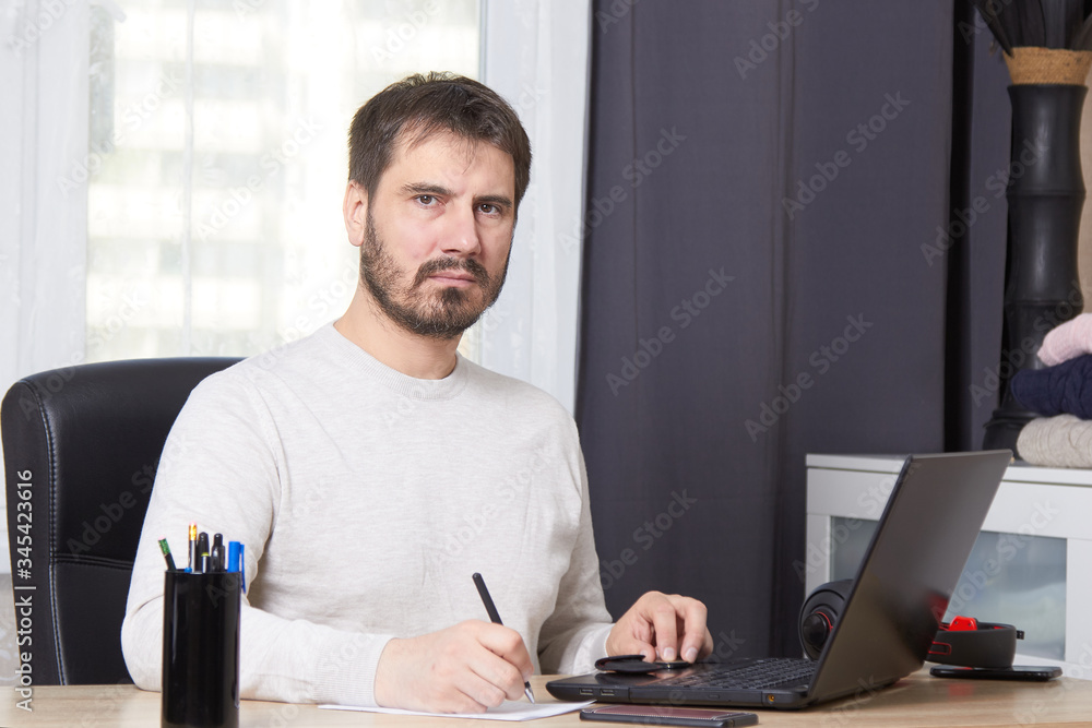 a bearded man is sitting at a Desk looking for work calling on his mobile