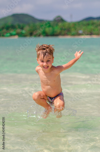  happy child splashes on the ocean. The kid smiles and bathes in the sea. Beautiful coast of the ocean, a child is played on the seashore. Boy at the sea. 
