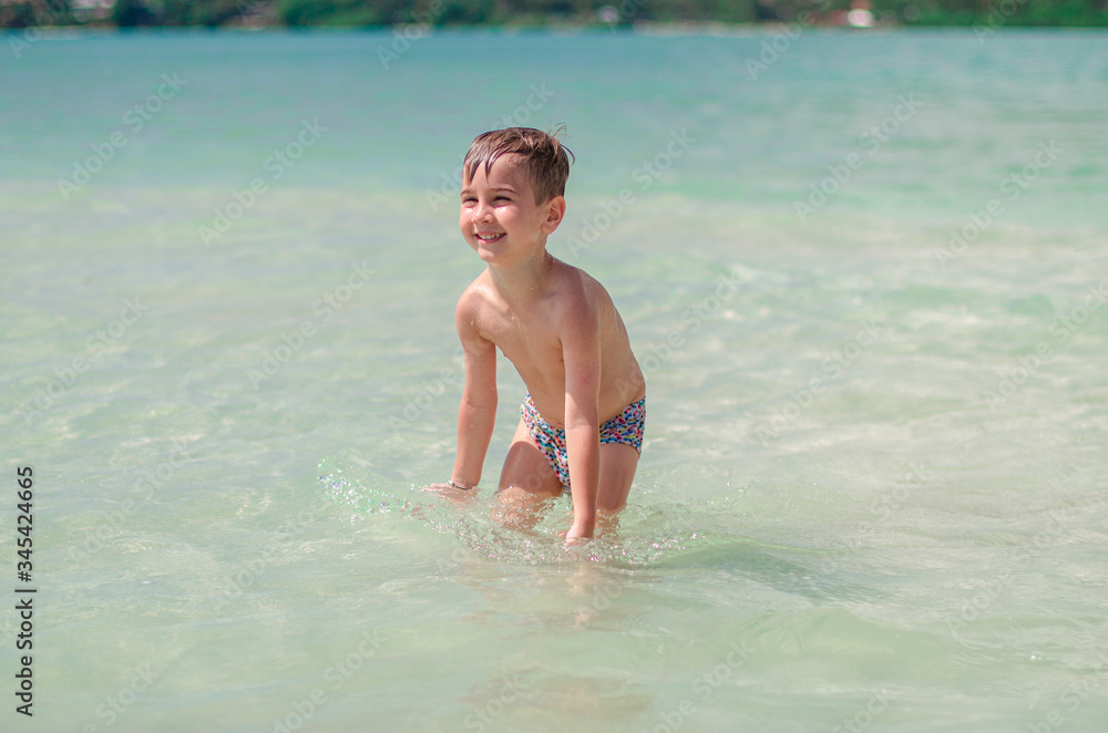 
happy child splashes on the ocean. The kid smiles and bathes in the sea. Beautiful coast of the ocean, a child is played on the seashore. Boy at the sea.
