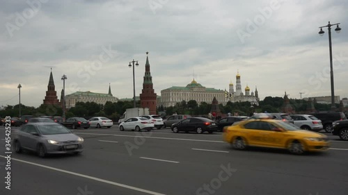 
View of passing vehicles from the Bolshoy Kamenny Bridge on a cloudy day. The Grand Kremlin Palace and The Ensemble of a Belltower of Ivan in the background.
