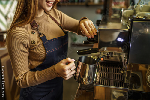 Cropped photo  young girl  barista steaming milk at the modern coffee shop