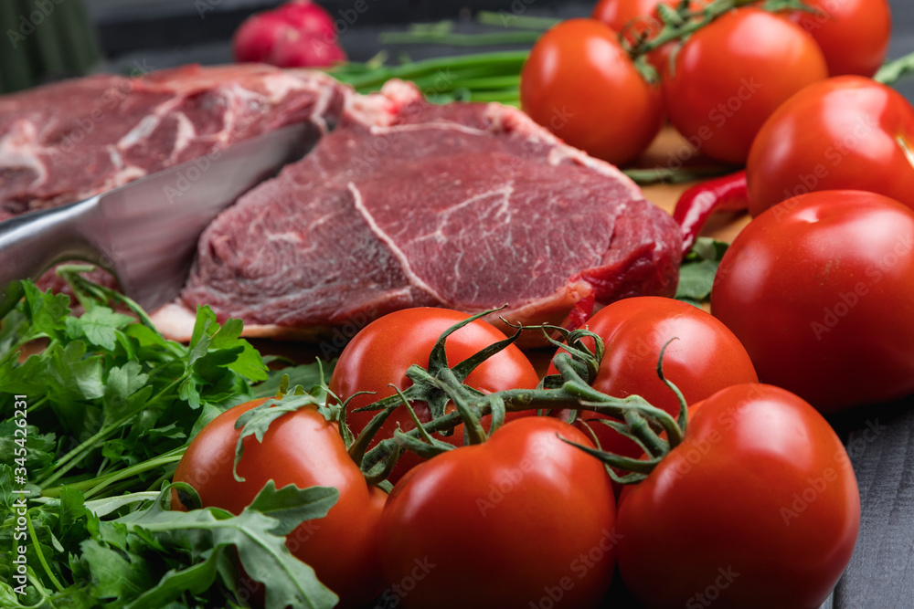 The preparation of fresh meat. Fresh beef steak on a wooden table. Meat surrounded by spices and vegetables. Fresh fruit. Red ripe tomatoes. Dietary food. The preparation of fresh meat. Fresh beef steak on a wooden table. Meat surrounded by spices and vegetables. Fresh fruit. Red ripe tomatoes. Dietary food.