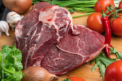 The preparation of fresh meat. Fresh beef steak on a wooden table. Meat surrounded by spices and vegetables. Fresh fruit. Red ripe tomatoes. Dietary food.