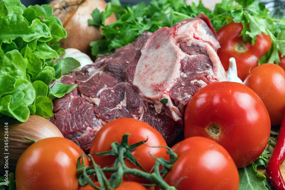 A piece of raw meat on a wooden cutting Board and various vegetables. Cooking meat. Fresh beef and ripe vegetables. Balanced diet. Natural protein.