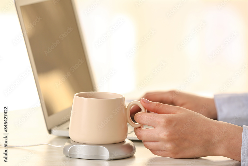 Woman taking cup of coffee from heater on table Woman taking cup of coffee from heater on table