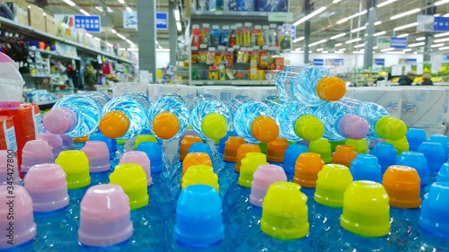 Sale of bottled water in a supermarket. Transparent plastic bottles with bright colorful caps. Blurred background of the interior of the store. Service Supplier. Environment concept. Natural resources photo