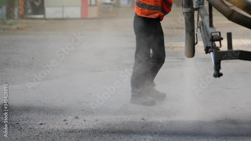 Workers perform minor repairs to pavement by spraying asphalt chips into pits on roadway. Machine blows hot bitumen mixture as road patches. Sealing cracks by blowing crushed granite stone with tar 