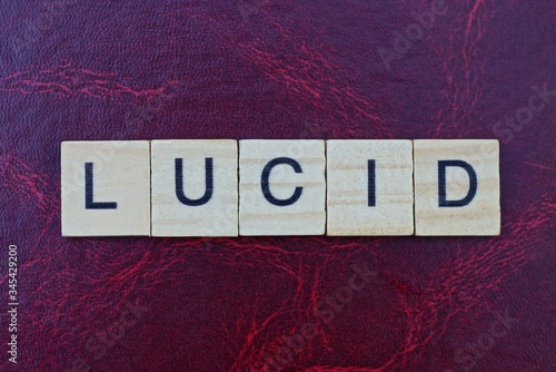 Tablou pe pânză text a word lucid from small gray wooden letters lies on a red table with a patt