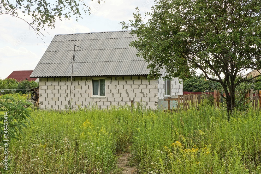 white private brick house with a window under a gray slate roof in green grass and trees in the summer garden white private brick house with a window under a gray slate roof in green grass and trees in the summer garden