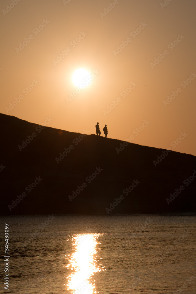 silhouette of two people walking on a hill at the beach at sunset
